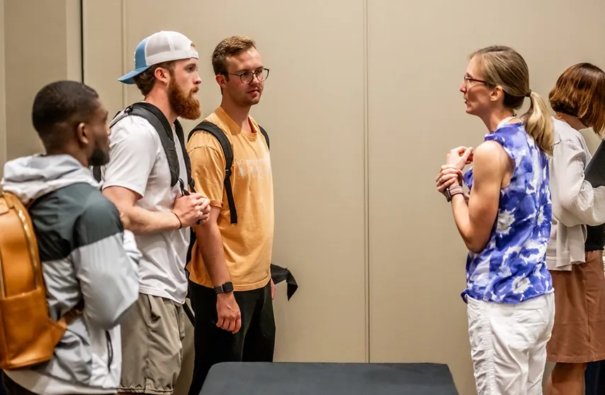 A woman stands and talks to a group of three students.